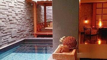 A modern indoor pool area with a stone wall, a lounge chair, and a small seating area with cushions and a table.