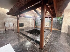 A spa area with a stone hot tub, wooden pillars, and a thatched roof structure. - Orient Luxury Villa Motel (Huwei)