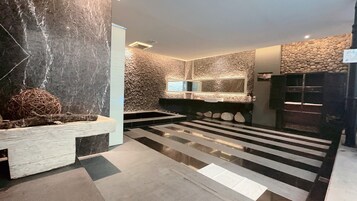 Un baño moderno con pared de piedra, banco de madera y un espejo grande.
