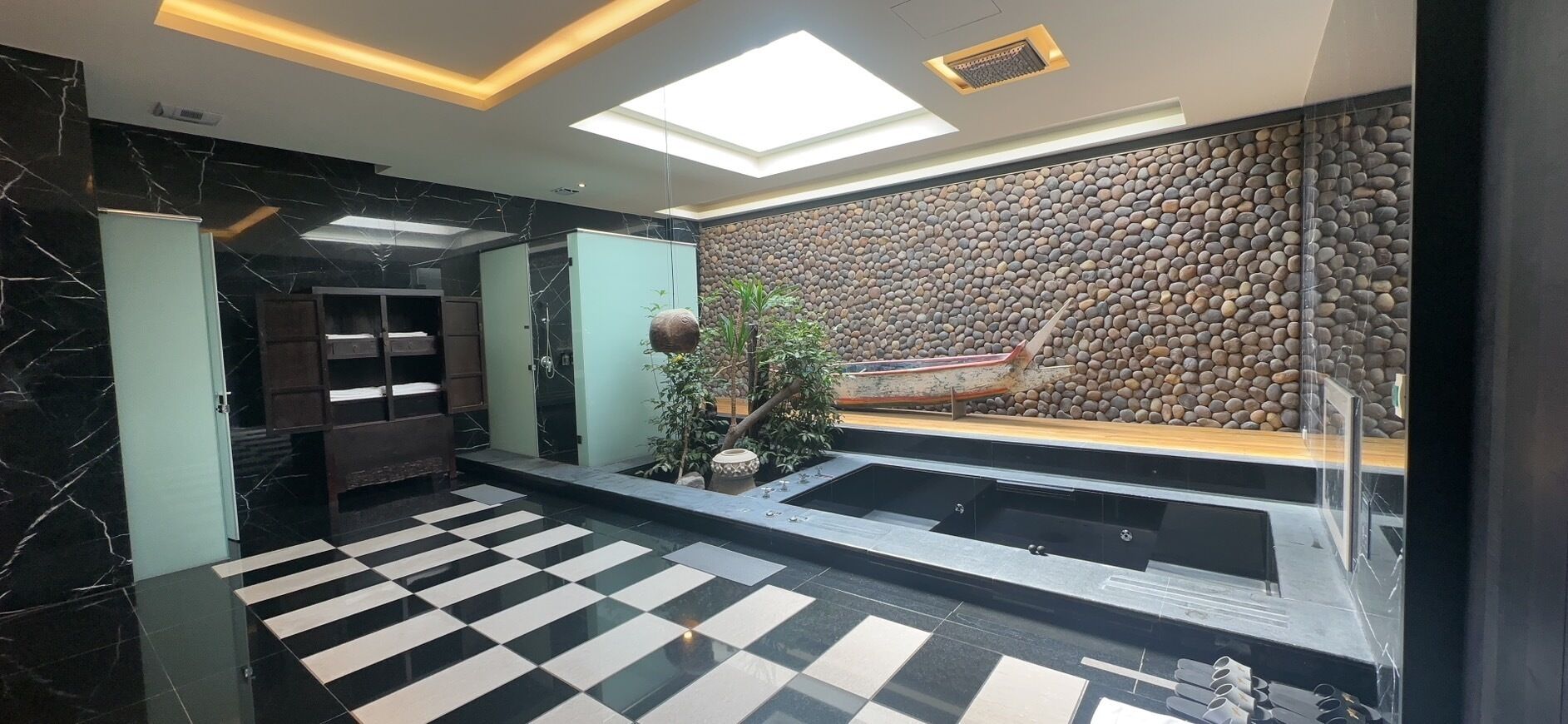 Eine moderne Lobby mit einem Schachbrettmuster-Boden, einer großen Felswand und einer Bootsausstellung.