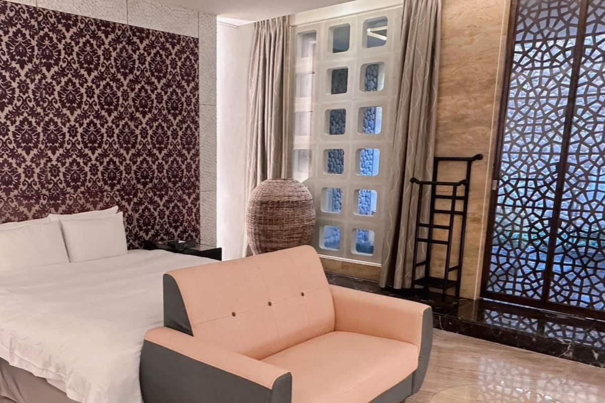 Quarto com cama, uma cadeira, janela ampla com vista e papel de parede estampado.