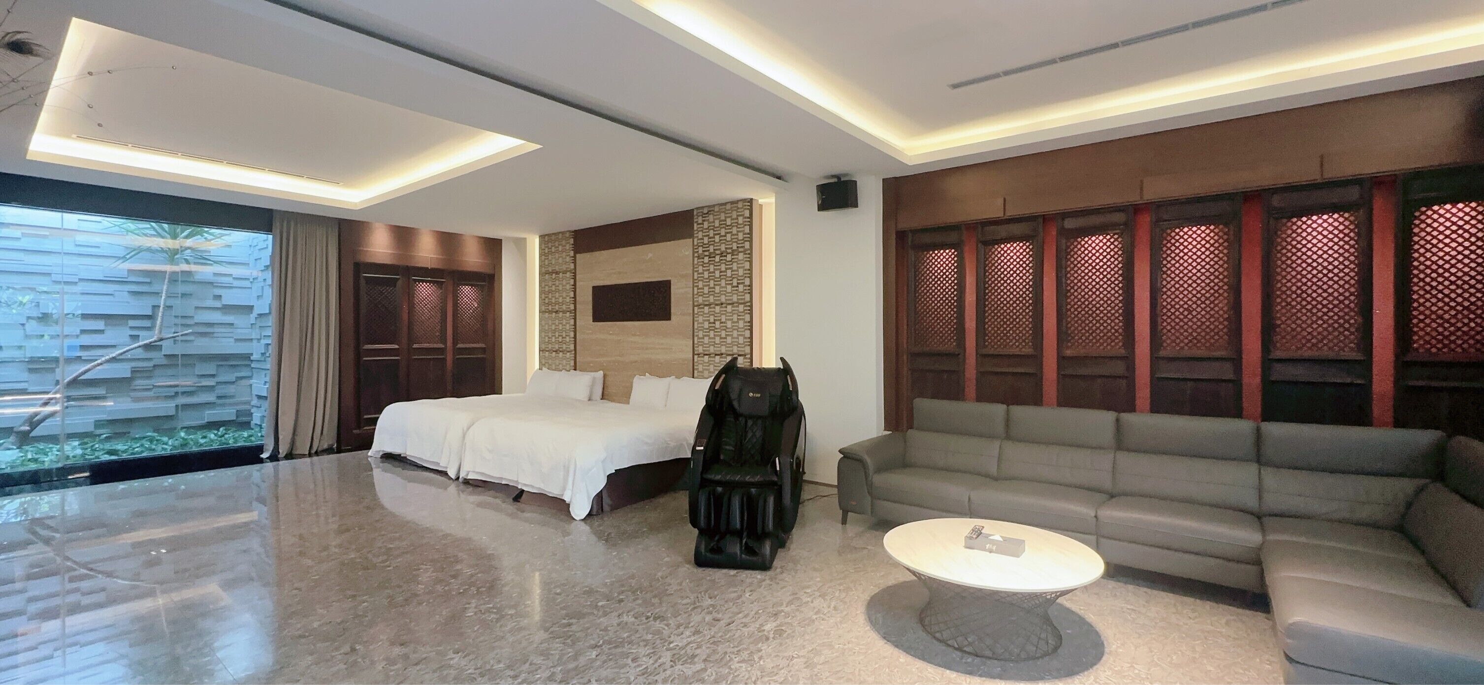 Una habitación de hotel moderna con una cama grande, un sofá, una silla de masaje y una mesita de café.