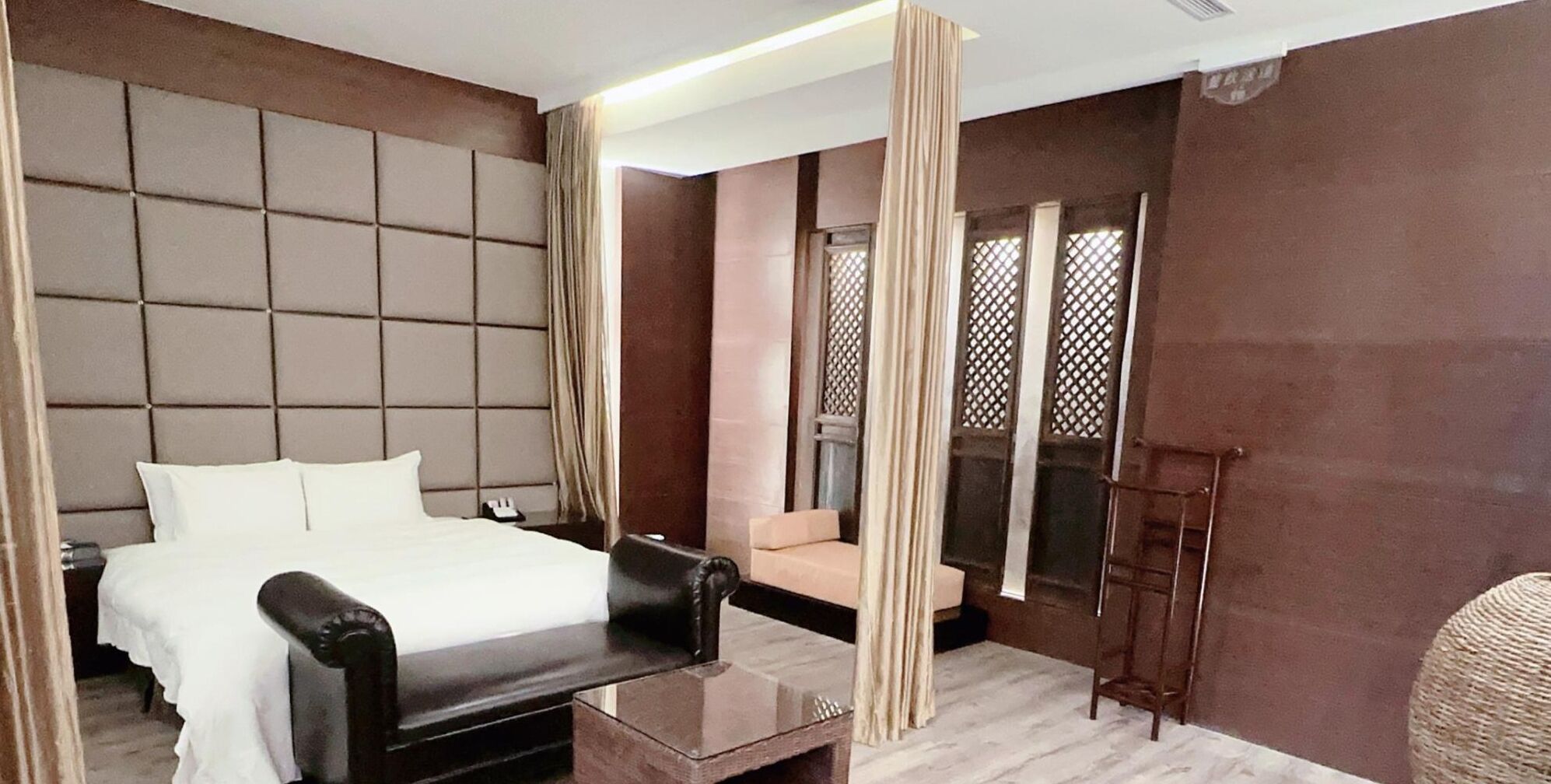 A modern hotel room with a large bed, a small sofa, a glass coffee table, and a chair.