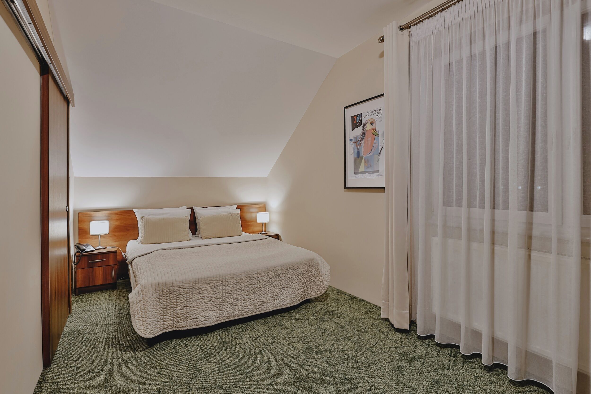 A hotel room with a bed, nightstand, lamp, and a framed picture on the wall.
