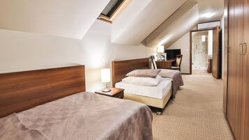 A hotel room with a sloped ceiling, two beds, a desk, a chair, a lamp, and a wardrobe.