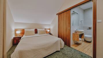 Habitación de hotel con cama, mesitas de noche, armario de madera y baño con lavamanos e inodoro.