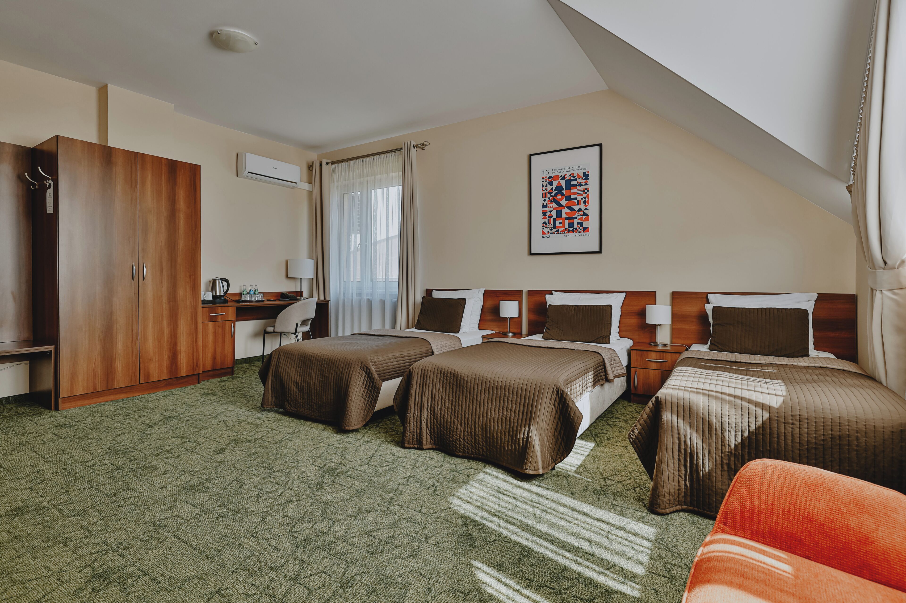 A hotel room with two beds, a desk, a wardrobe, and a large window with curtains.