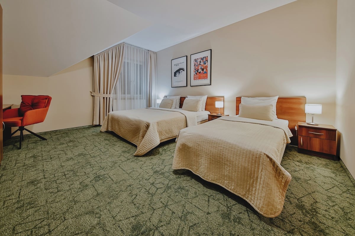 A hotel room with two beds, a desk, a chair, a nightstand, and a window with curtains.