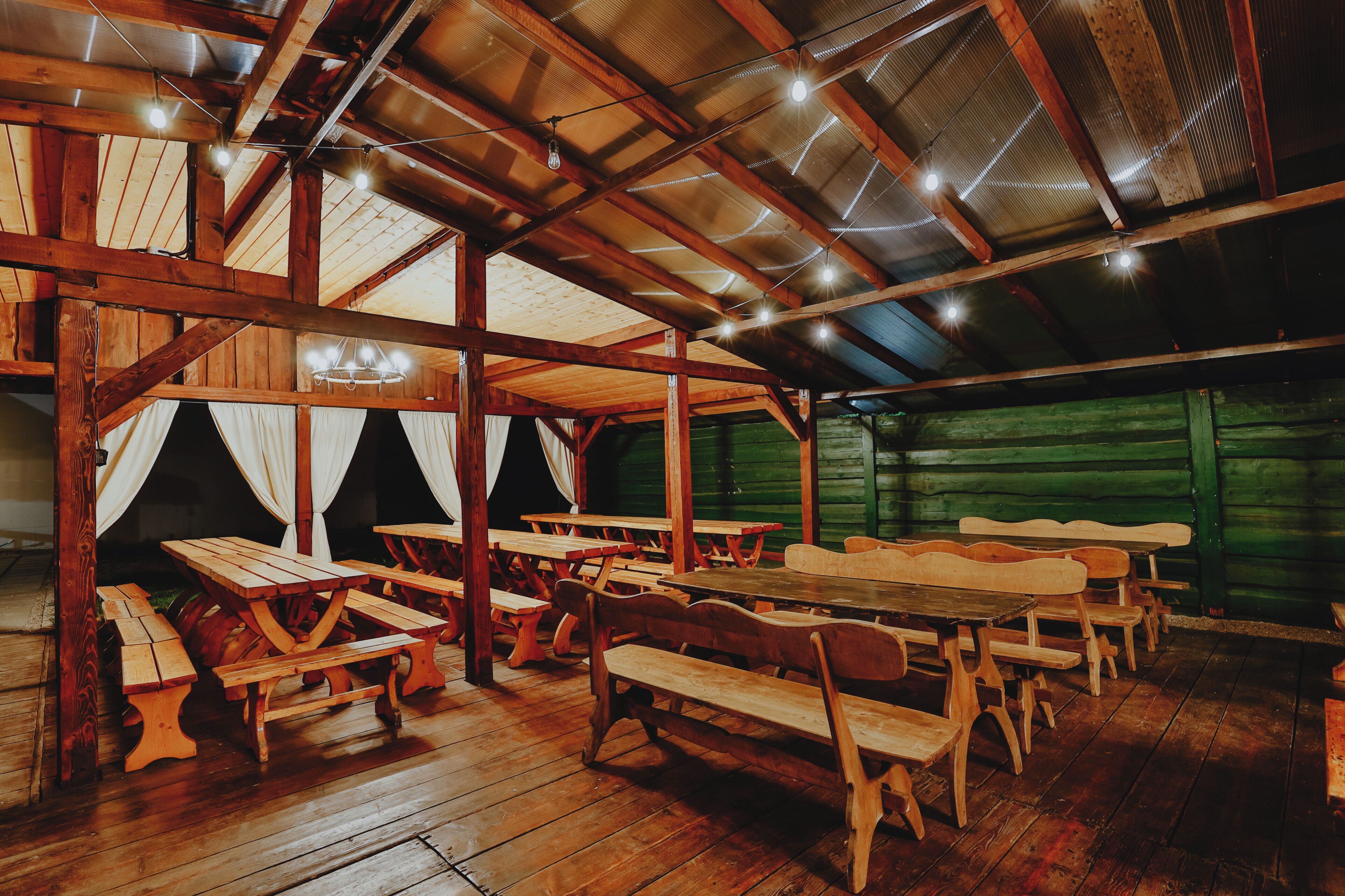 Un interior rústico de madera con varias mesas de picnic y bancos, un techo alto con vigas a la vista y una pared verde.