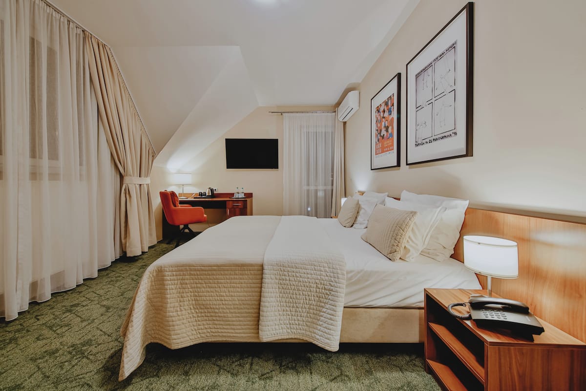 A hotel room with a bed, a desk, a chair, a TV, and artwork on the walls.