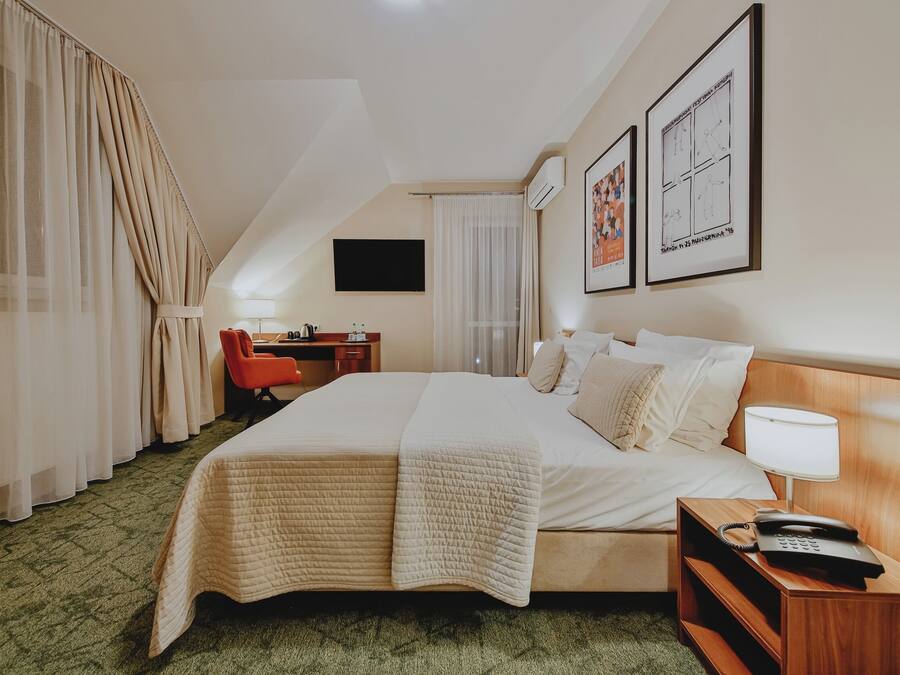 Una habitación de hotel con cama, escritorio, silla, televisor y obras de arte en la pared.
