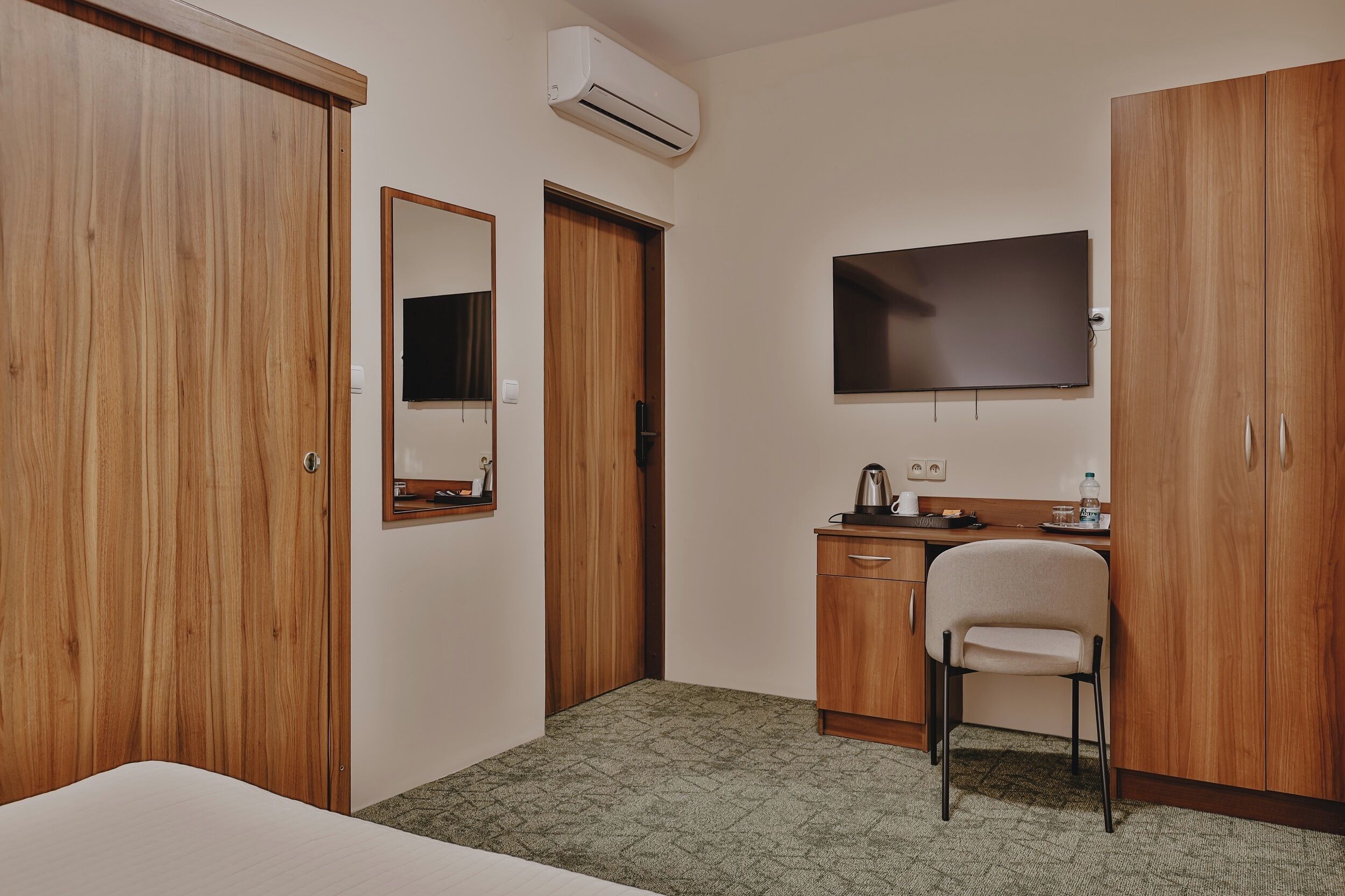 A hotel room with a bed, a desk with a chair, a television, and wooden wardrobes.