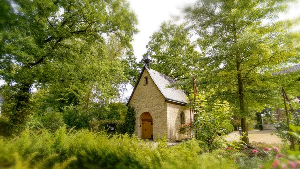 A small stone building with a single arched entrance, surrounded by lush greenery and trees. - Haus Mariengrund (Münster)