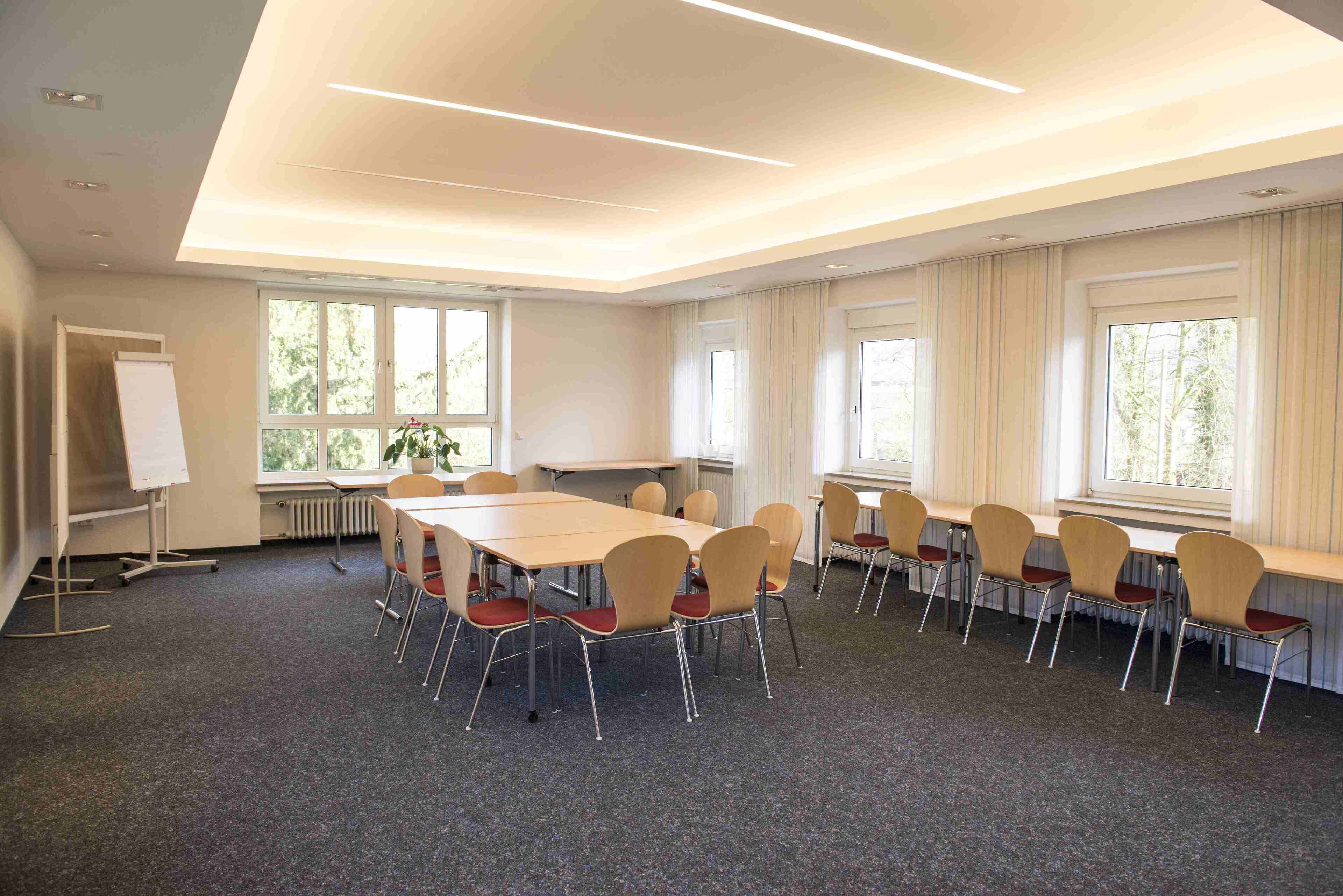 Une salle de conférence équipée d’une grande table, de chaises, d’un tableau blanc et de grandes fenêtres.