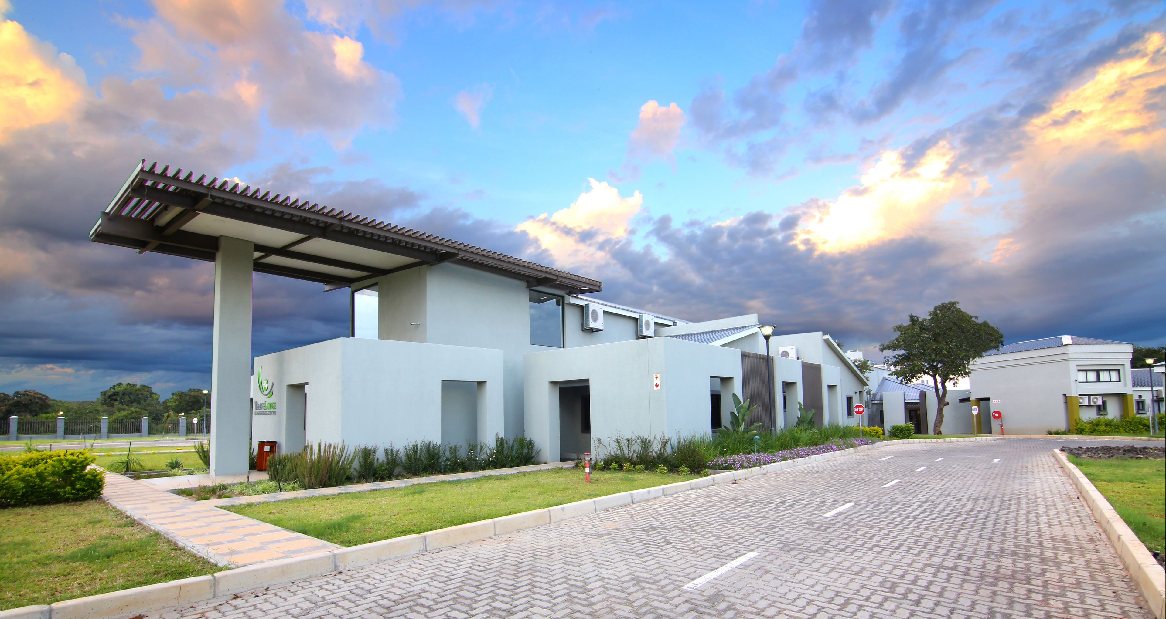 A modern building with a covered entrance, paved walkway, and landscaped garden.