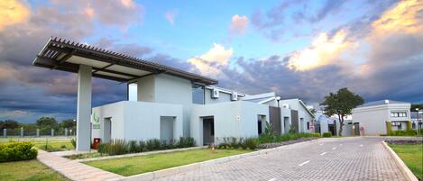 A modern building with a covered entrance, paved walkway, and landscaped garden.