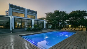 A modern pool area with a wooden deck, a pool, and a building with large windows and a staircase. - Travelodge Kasane (Kasane)