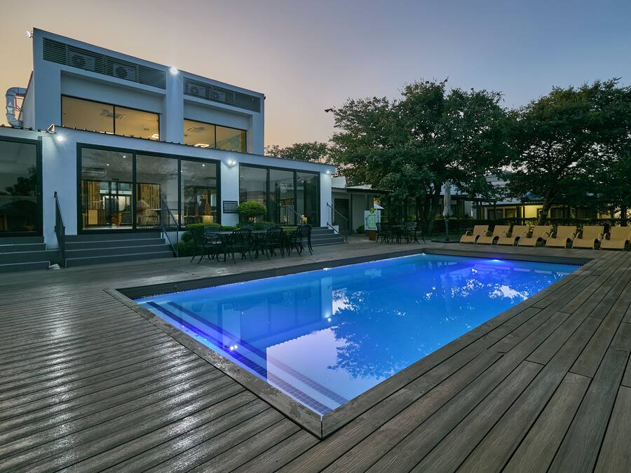A modern pool area with a wooden deck, a pool, and a building with large windows and a staircase.