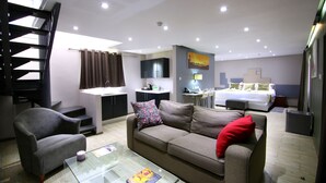 A modern hotel room with a sofa, armchair, glass coffee table, and a bed with a headboard. - Travelodge Kasane (Kasane)