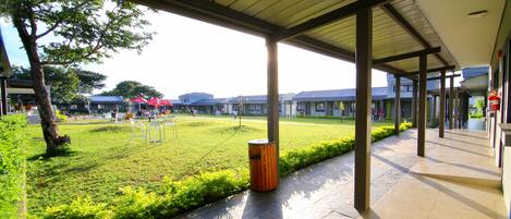 A covered outdoor area with a grassy lawn, metal chairs, and a trash can.