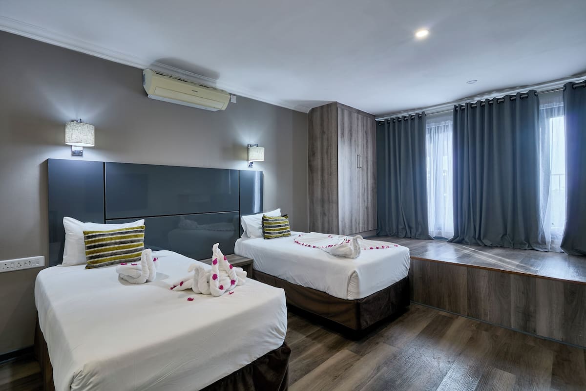 A hotel room with two beds, a large window with curtains, and an air conditioning unit on the wall.