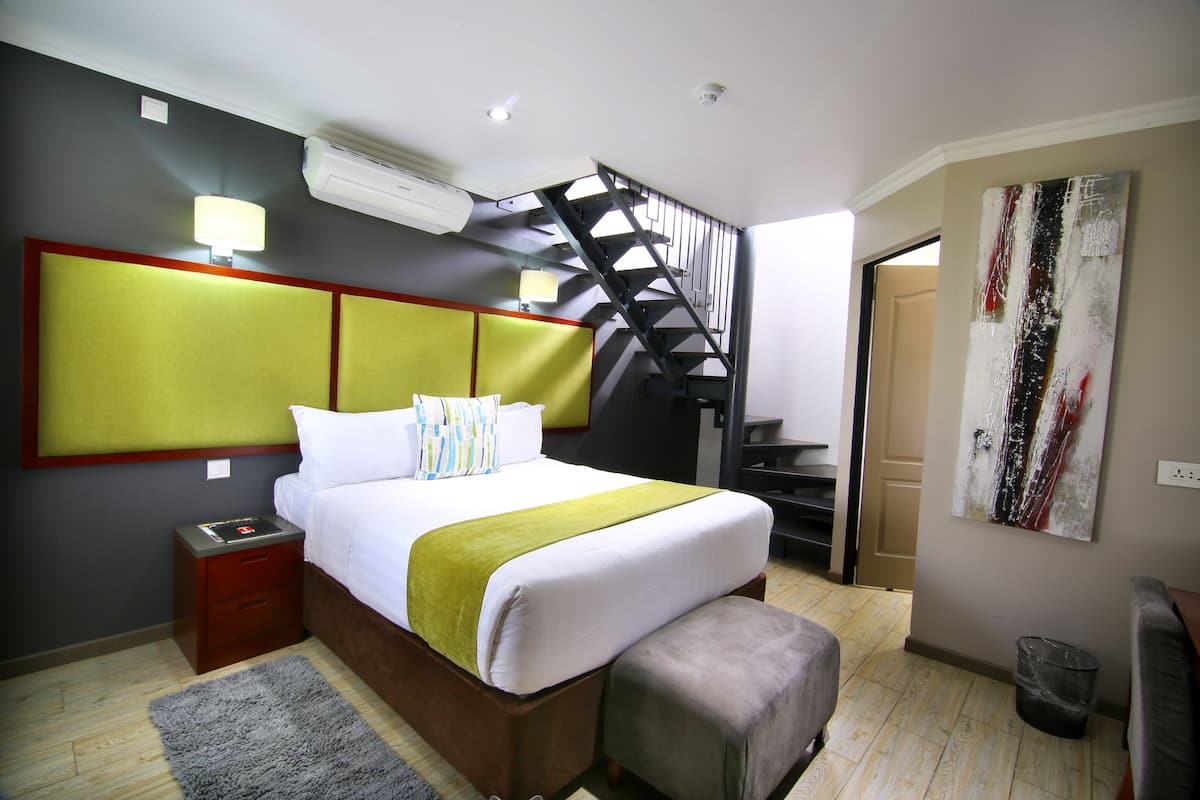 A bedroom with a bed, a nightstand, a grey rug, a staircase, and a painting on the wall.