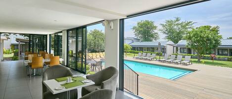 Un comedor moderno con amplias ventanas que dan a una piscina y un espacio de estar exterior.