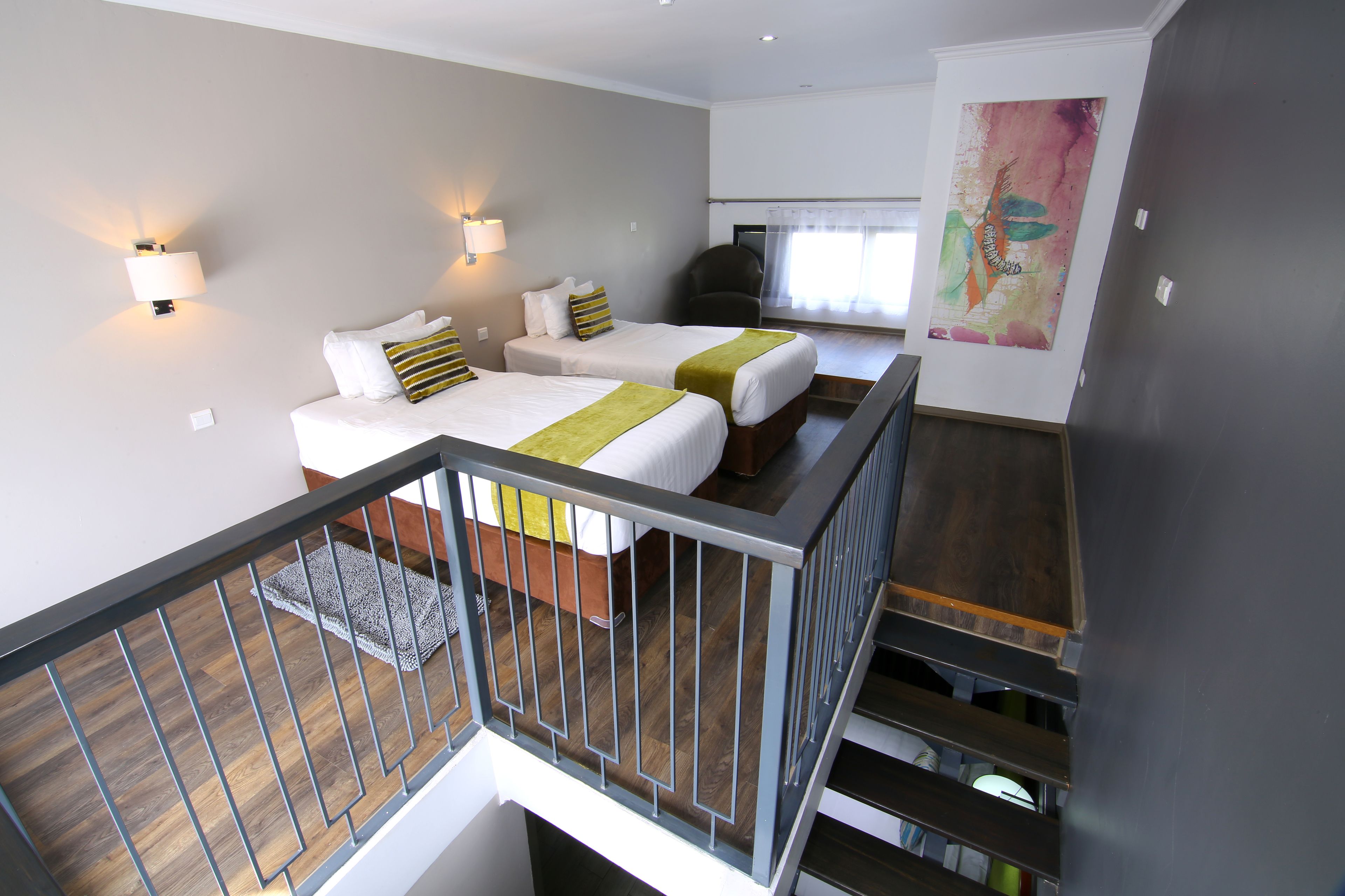 Habitación de hotel con dos camas, una escalera y un cuadro abstracto grande en la pared.