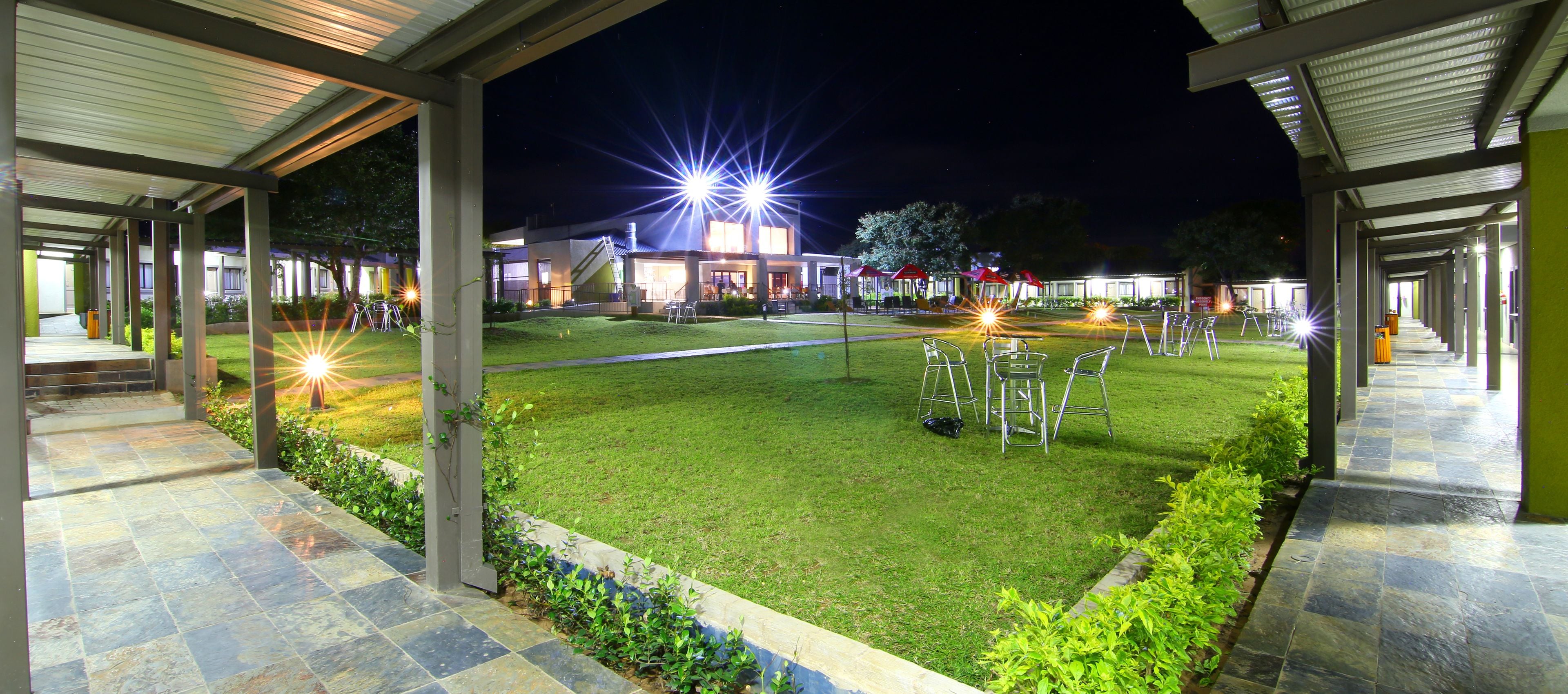 A well-lit outdoor area with a grassy lawn, metal chairs, and a building with bright lights.