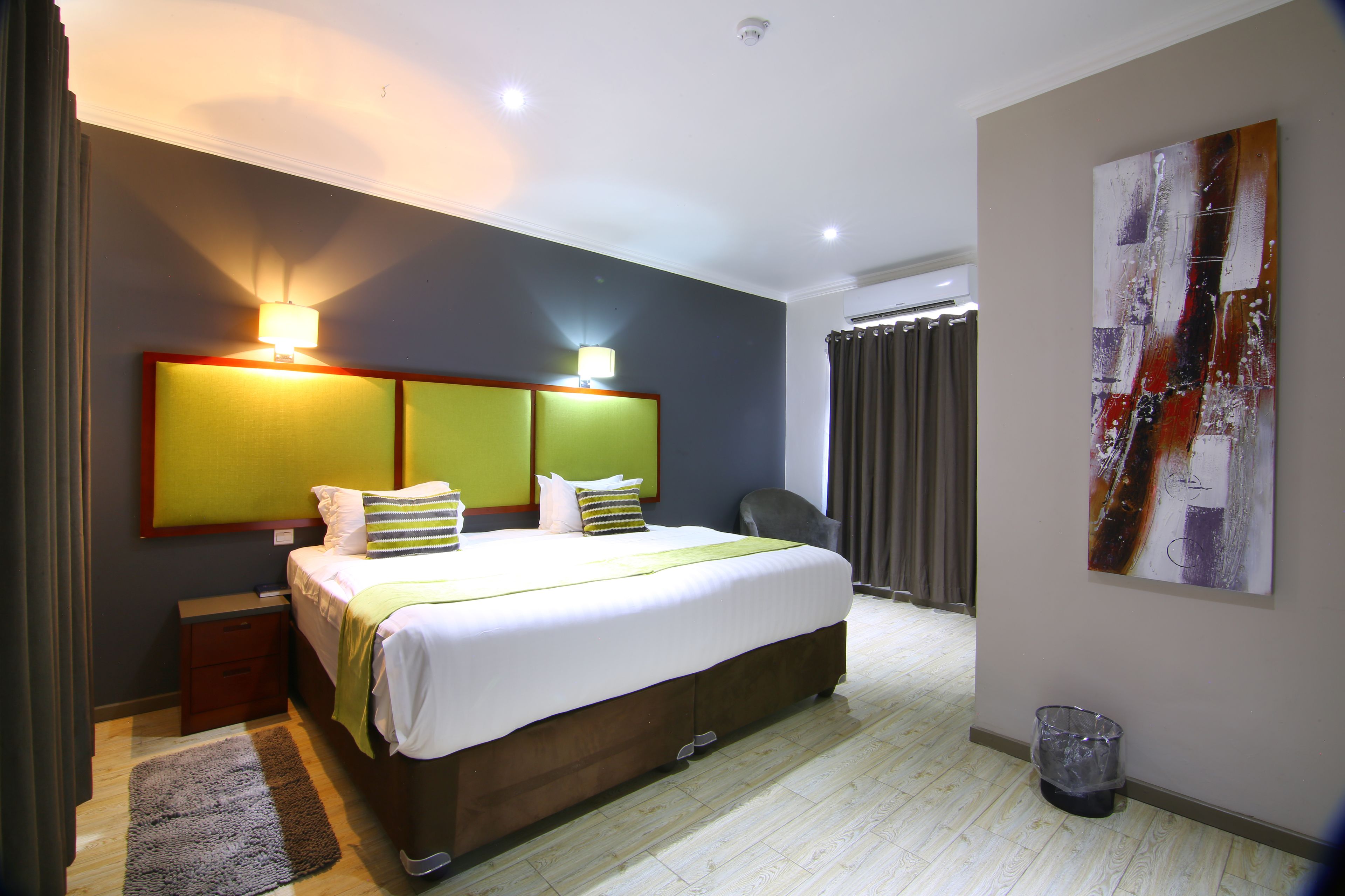 A modern hotel room with a large bed, bedside lamps, a chair, and a trash bin.