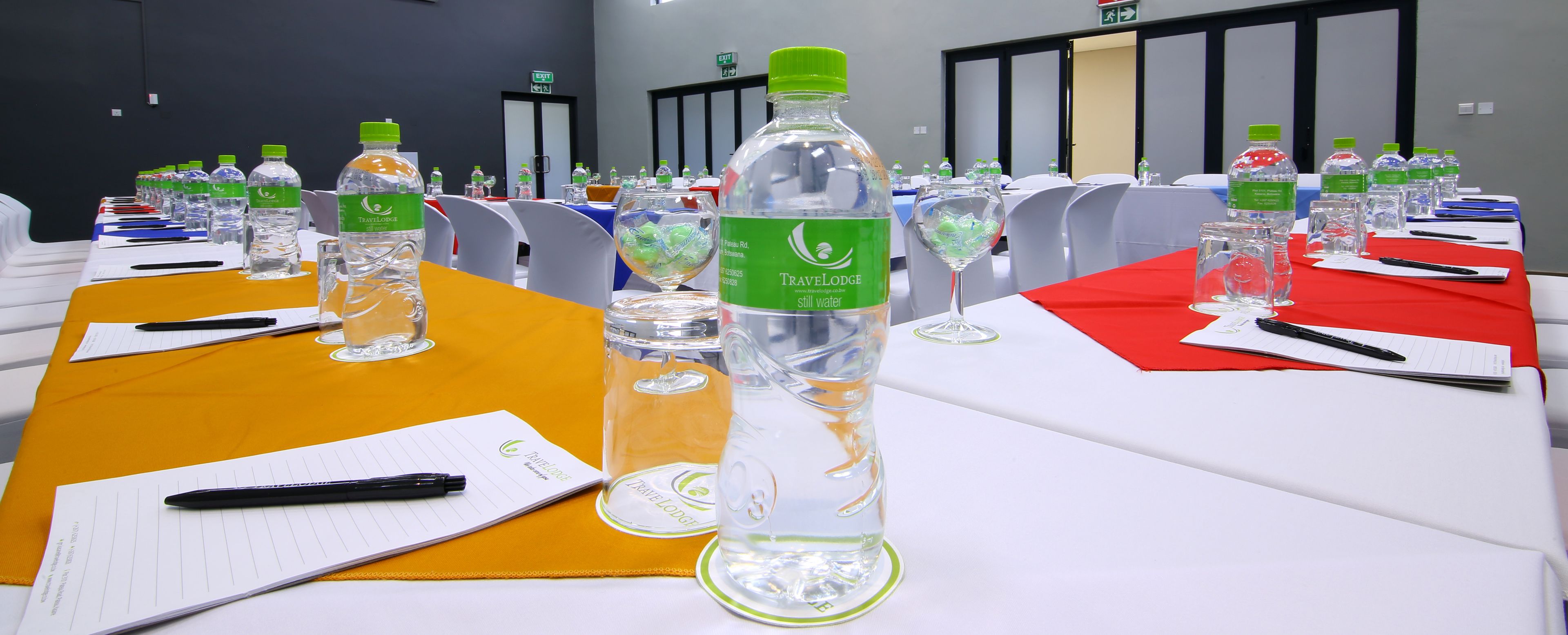 Un salón de conferencias con mesas dispuestas para una reunión, cada una con placas de identificación, botellas de agua y blocs de notas.