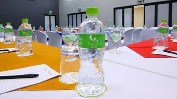 Un salón de conferencias con mesas dispuestas para una reunión, cada una con placas de identificación, botellas de agua y blocs de notas.