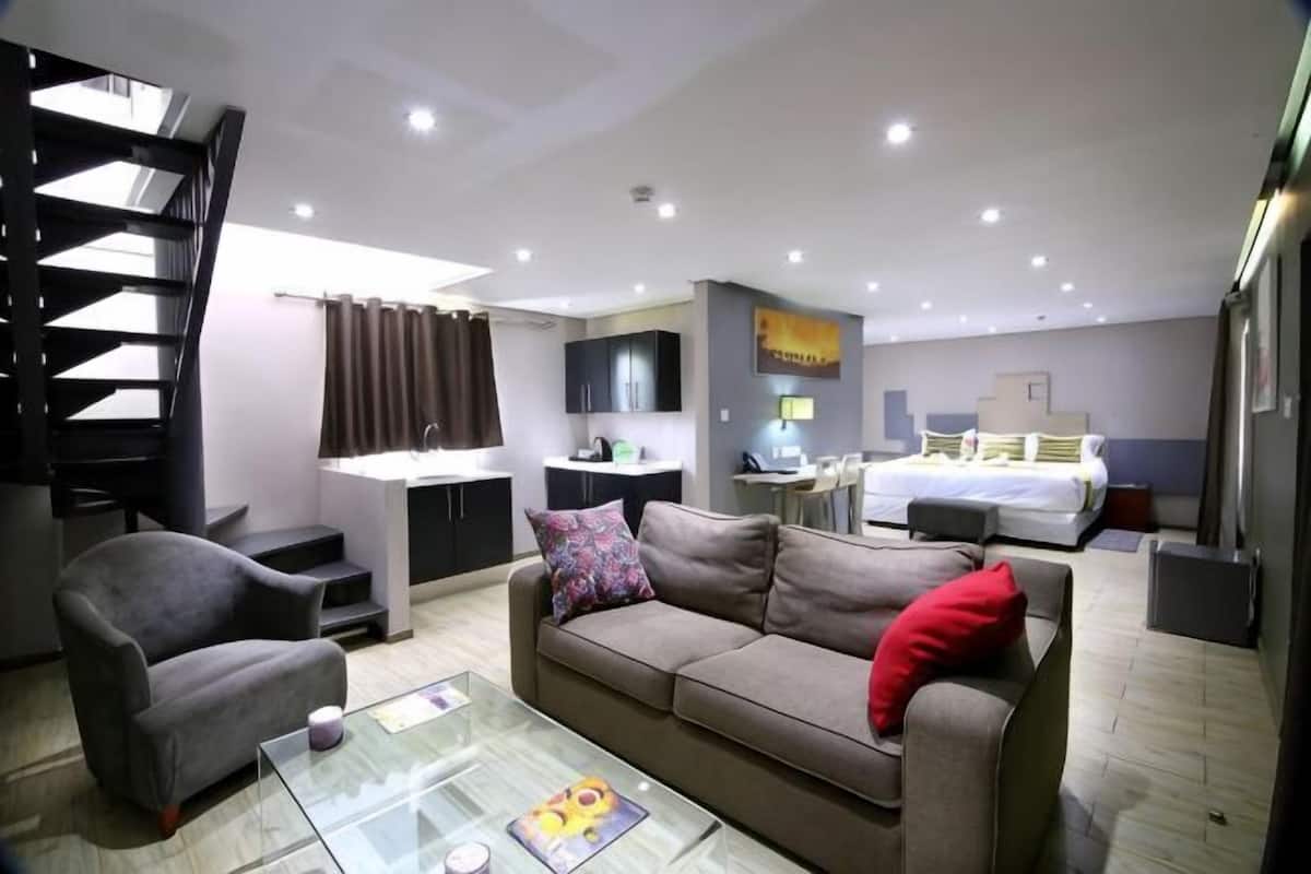 A modern living room with a sofa, armchair, and glass coffee table. A staircase is visible in the background.