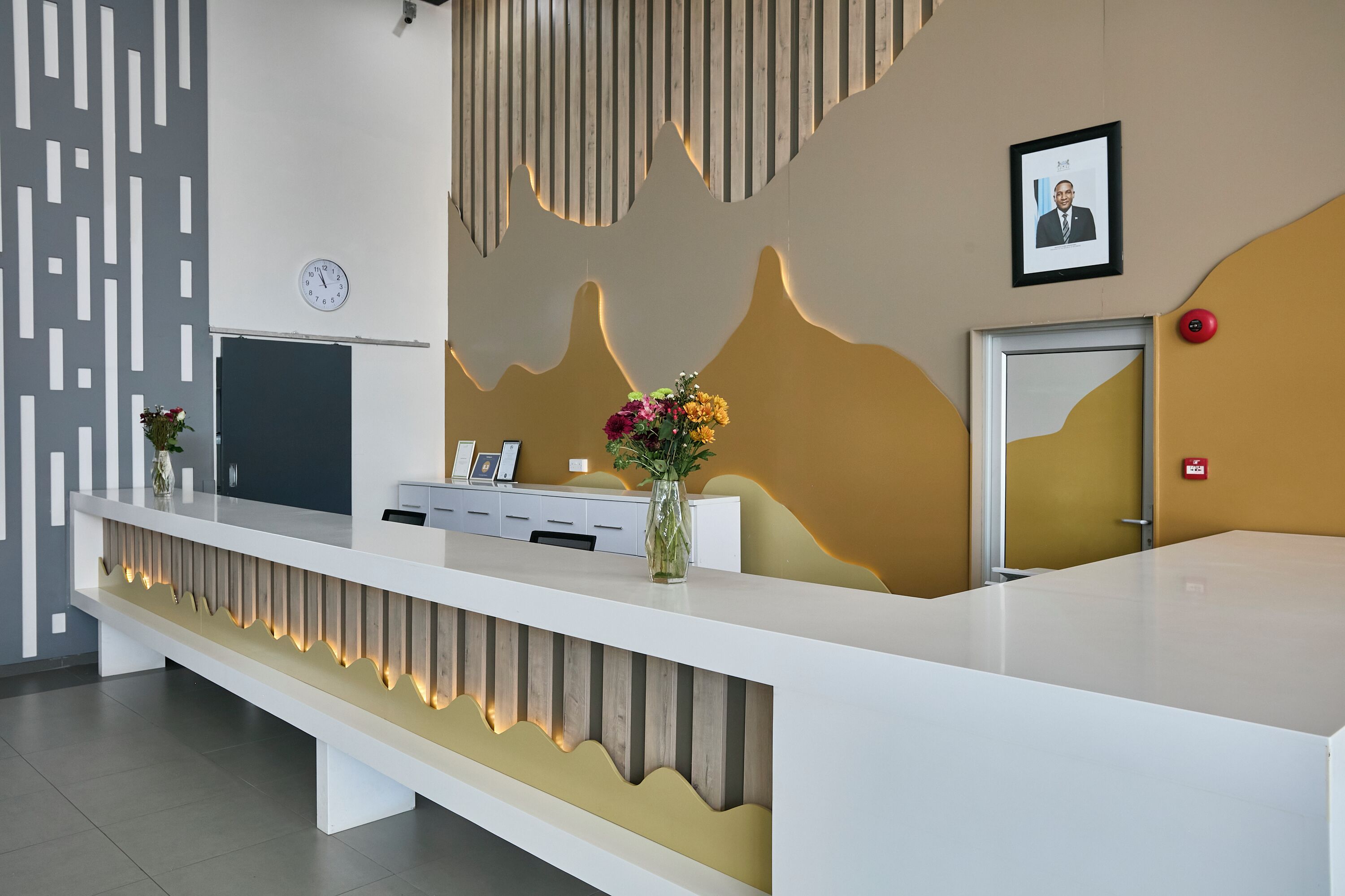 A reception desk with a clock, framed photos, and a vase with flowers.