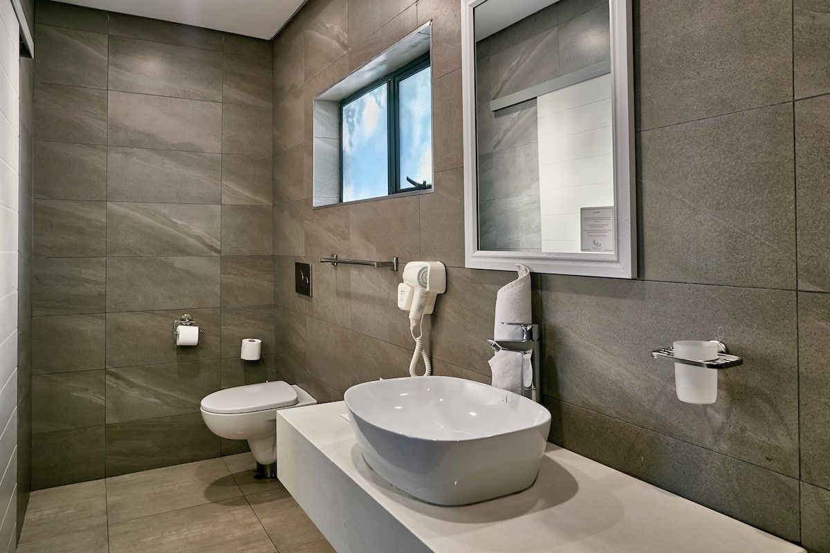 A modern bathroom with a large vessel sink, a toilet, a hairdryer, and a towel rack.