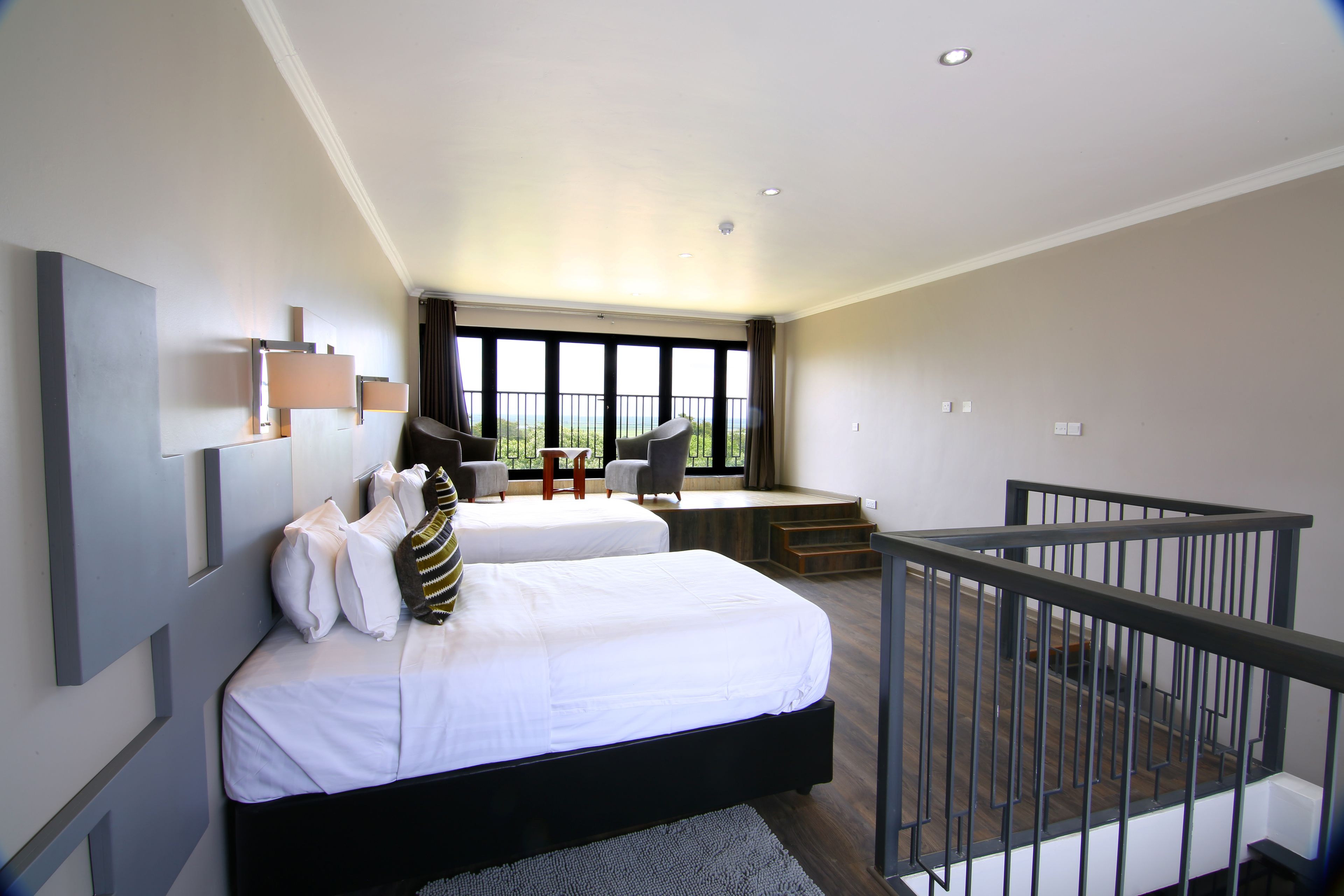 A modern hotel room with a large bed, a desk, and a balcony with a view.