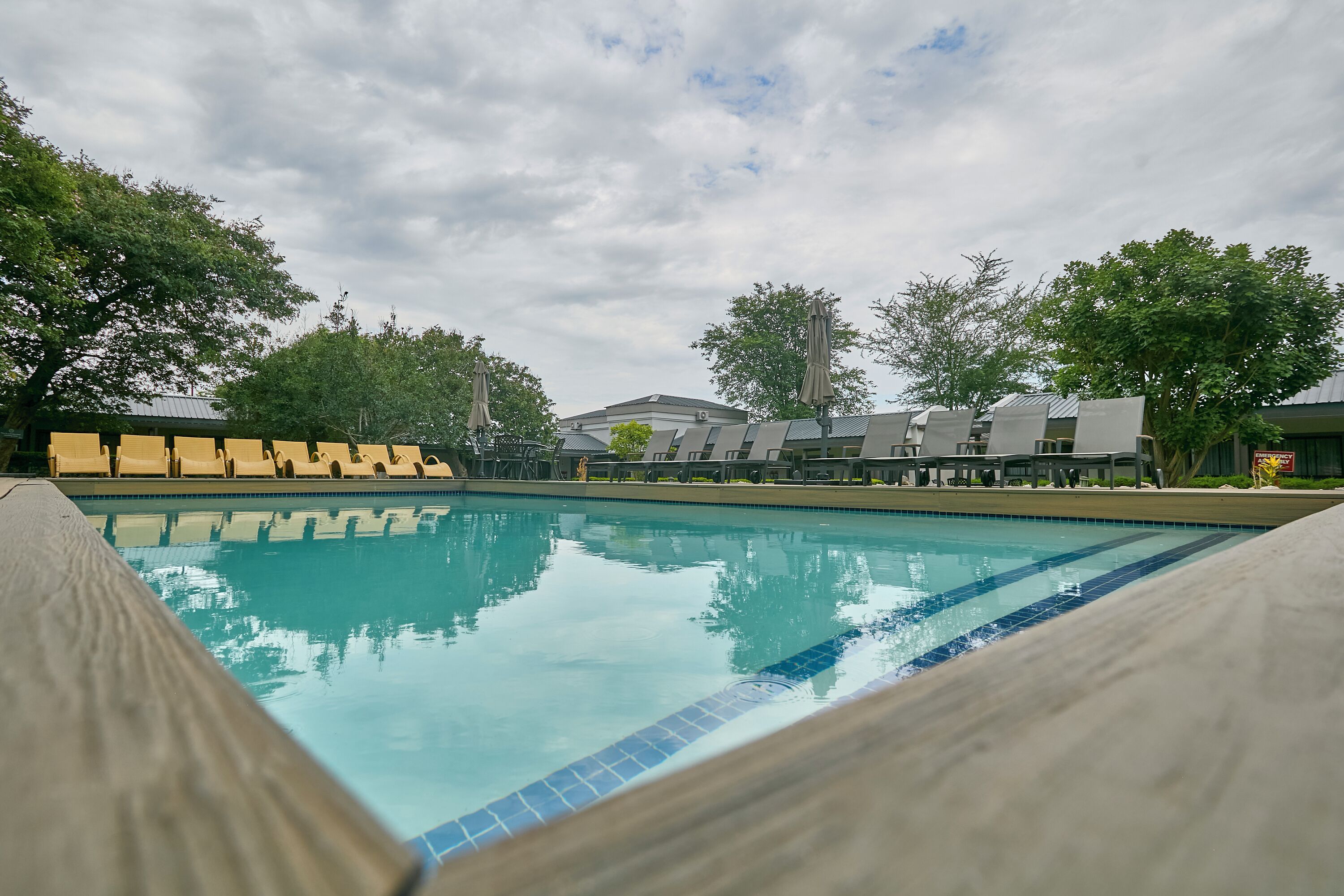 A swimming pool with lounge chairs and umbrellas, surrounded by trees and buildings.