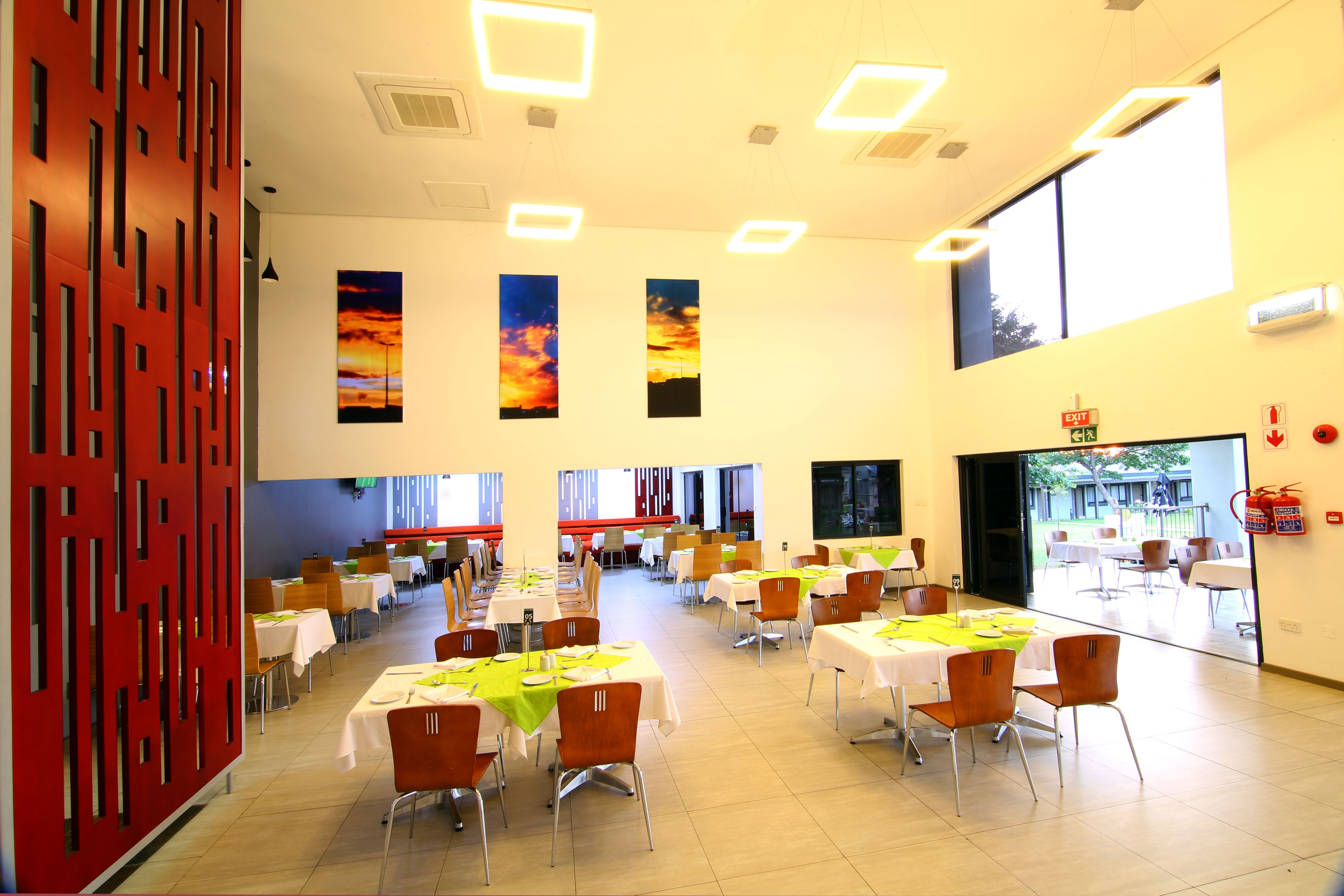 A spacious dining area with multiple tables and chairs, large windows, and a red partition wall.