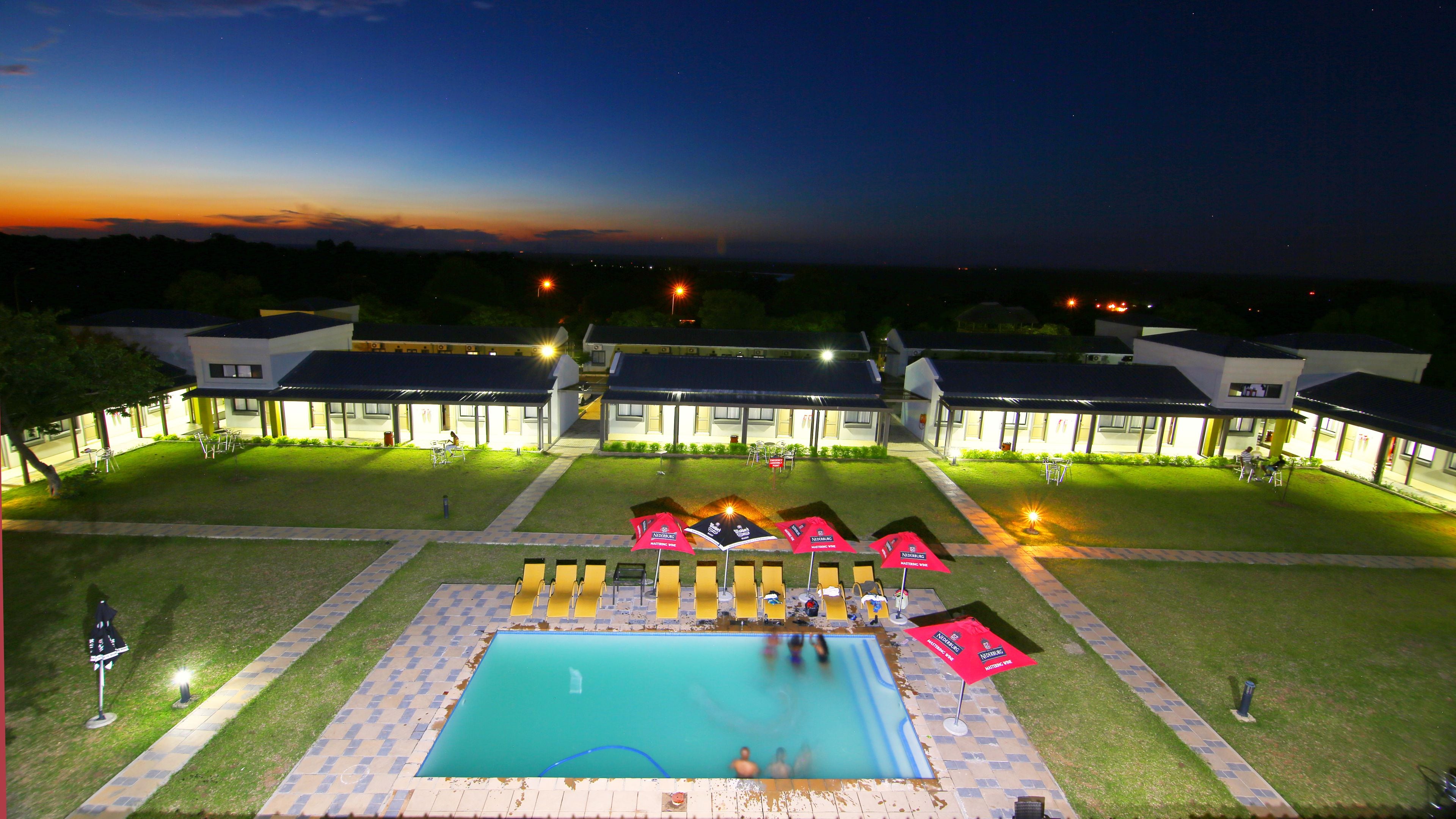 Ein Hotel mit Schwimmbad, Außenbereich zum Sitzen und gut beleuchteten Gebäuden.