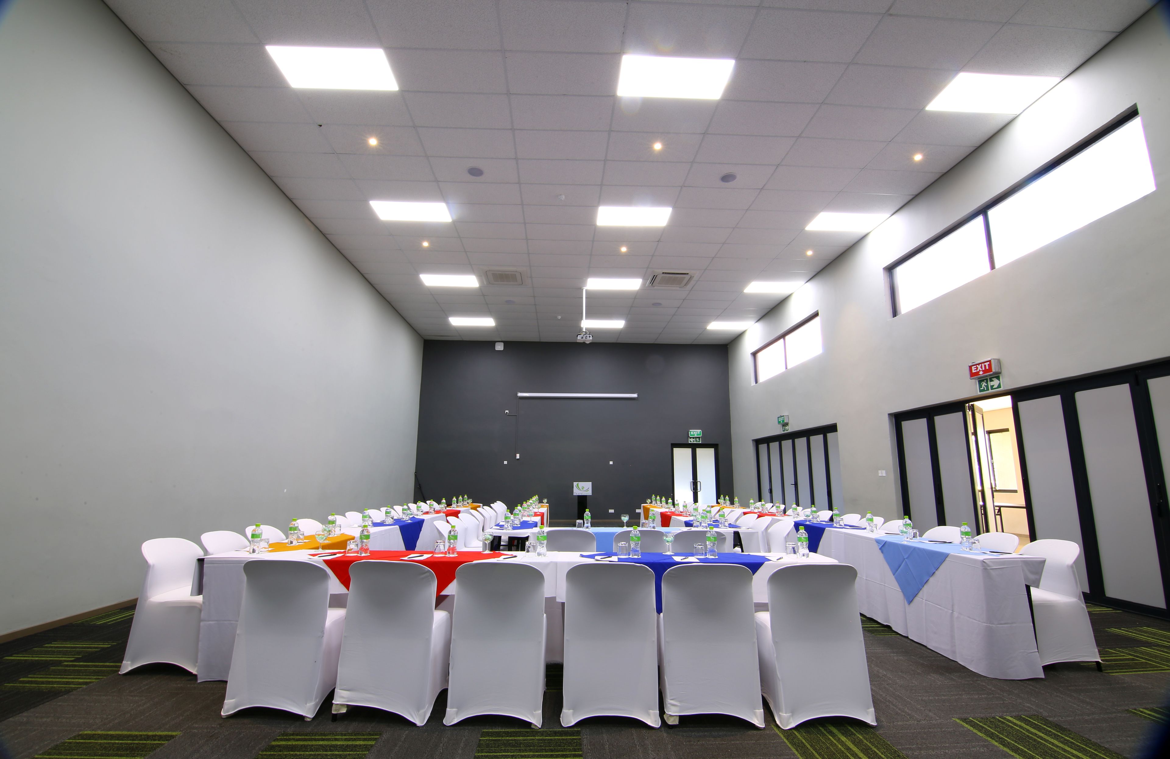 A conference room with multiple tables, white chairs, and a projector screen.