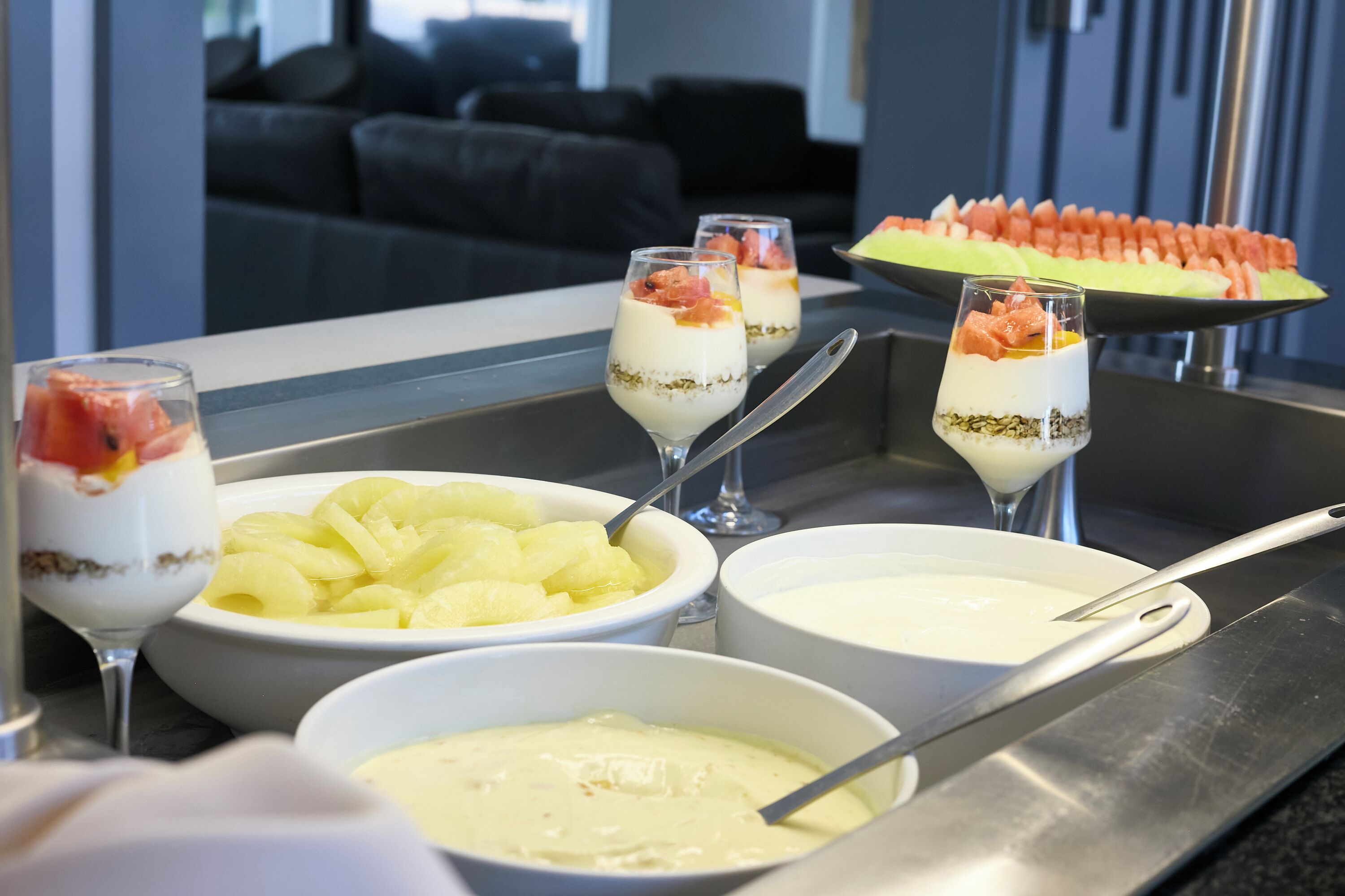 A buffet with various dishes including fruit, yogurt parfaits, and a watermelon dish.
