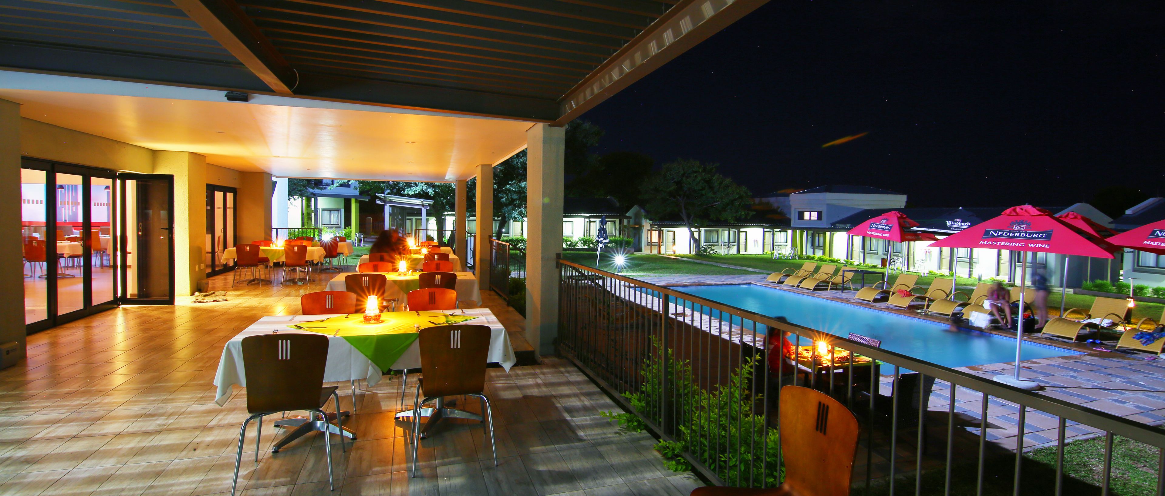An outdoor dining area with tables and chairs, a poolside lounge with umbrellas, and a view of the pool and surrounding buildings.