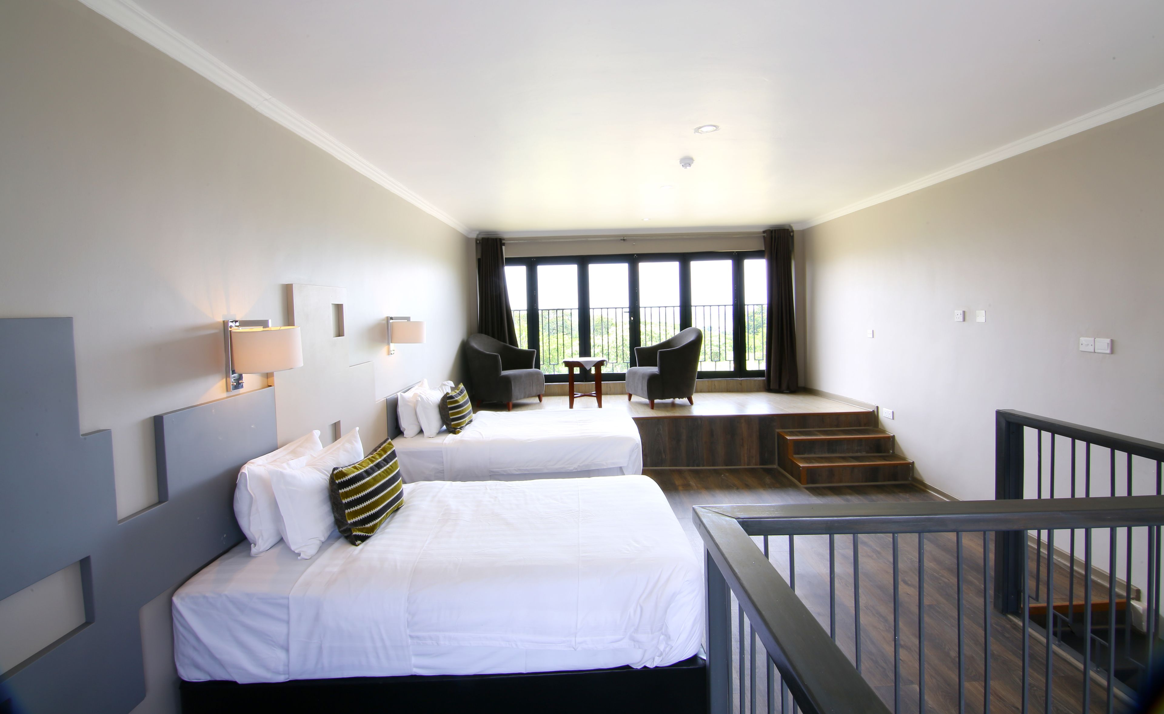 A hotel room with two beds, a small table, and a balcony with a view.