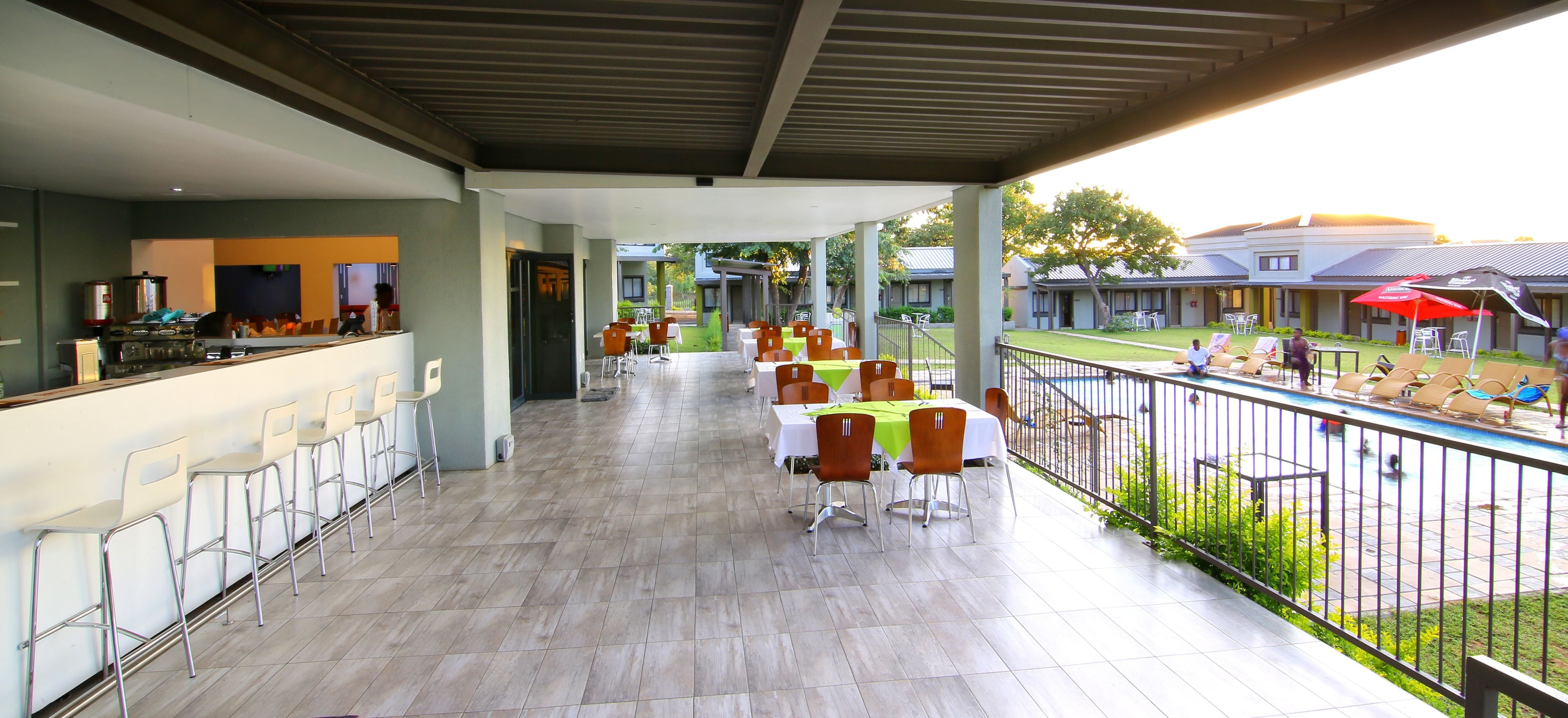 Un espace extérieur abrité comprenant un bar, des tables et des chaises. On y trouve également une piscine avec des chaises longues et des parasols.