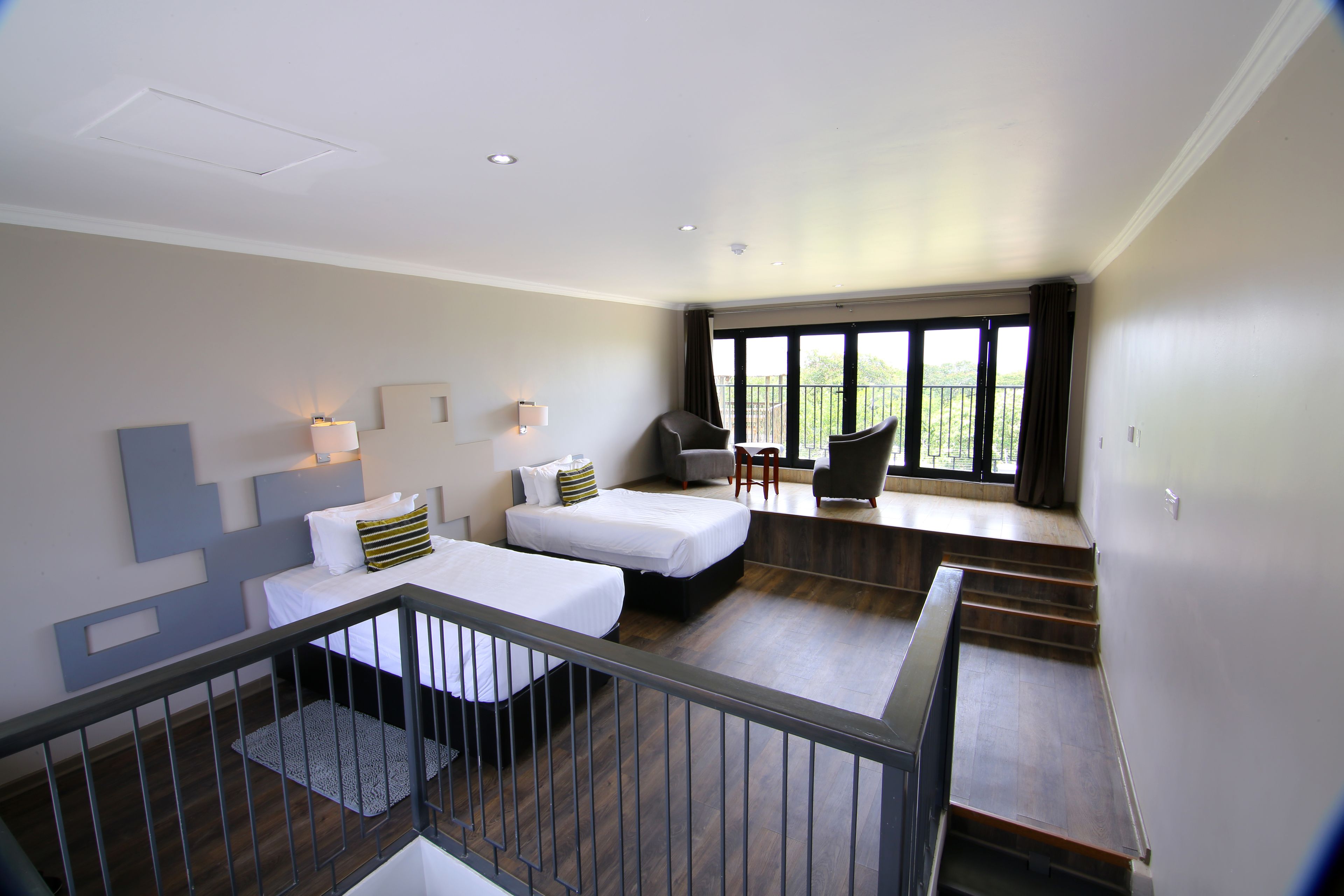 A modern hotel room with two beds, a balcony, and a view of greenery.