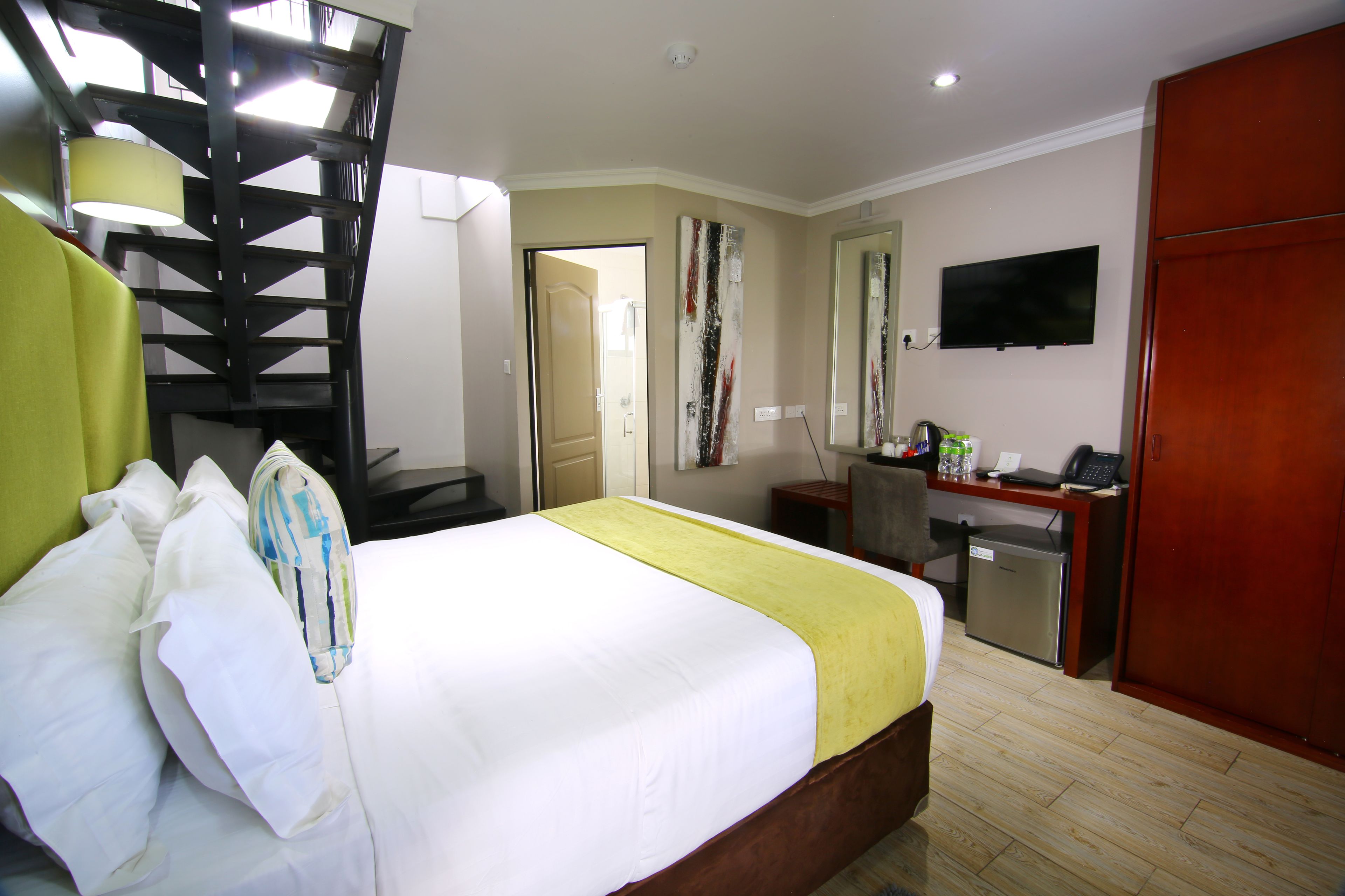 Una camera d'albergo con un letto, una scrivania, un computer, una TV e una scala.