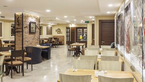 A restaurant with multiple seating areas, including booths and tables, with a brick accent wall and a large menu display. - Hotel Antroyal (Antalya)