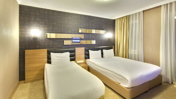 Quarto de hotel com duas camas, parede escura com padrão e luminária moderna.