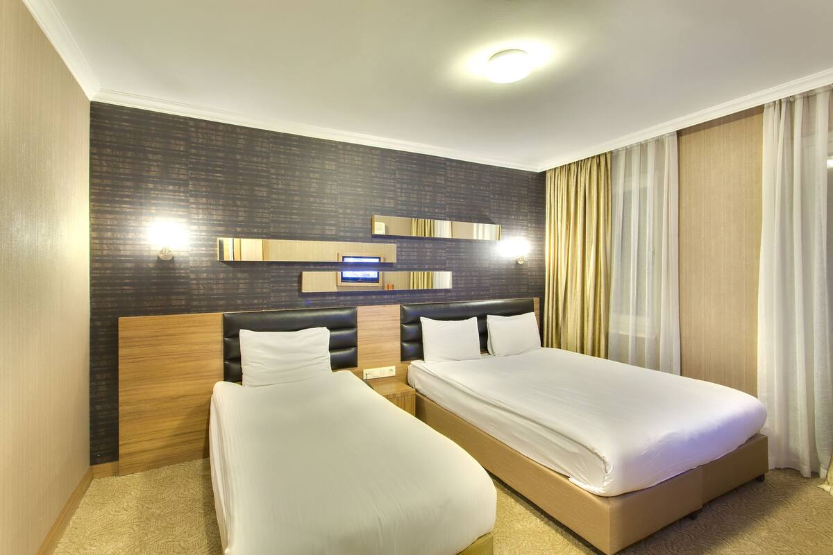 A hotel room with two beds, a dark patterned wall, and a modern light fixture.