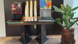 A reception area with a coffee machine, stacked white cups, and a potted plant. - Hotel Antroyal (Antalya)